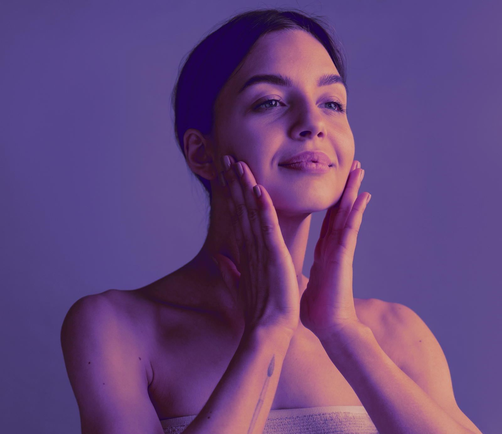 Tu tipo de piel Mujer joven tocando su rostro con ambas manos, piel limpia y luminosa, en un fondo morado, rutina de skincare facial.